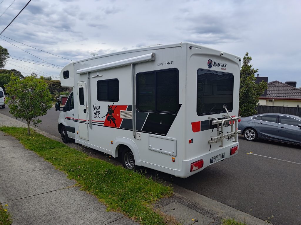 Rear three-quarter view of the Mobile Dojo after branding, showing the NinjaWeb wrap applied across the back and side panels.
